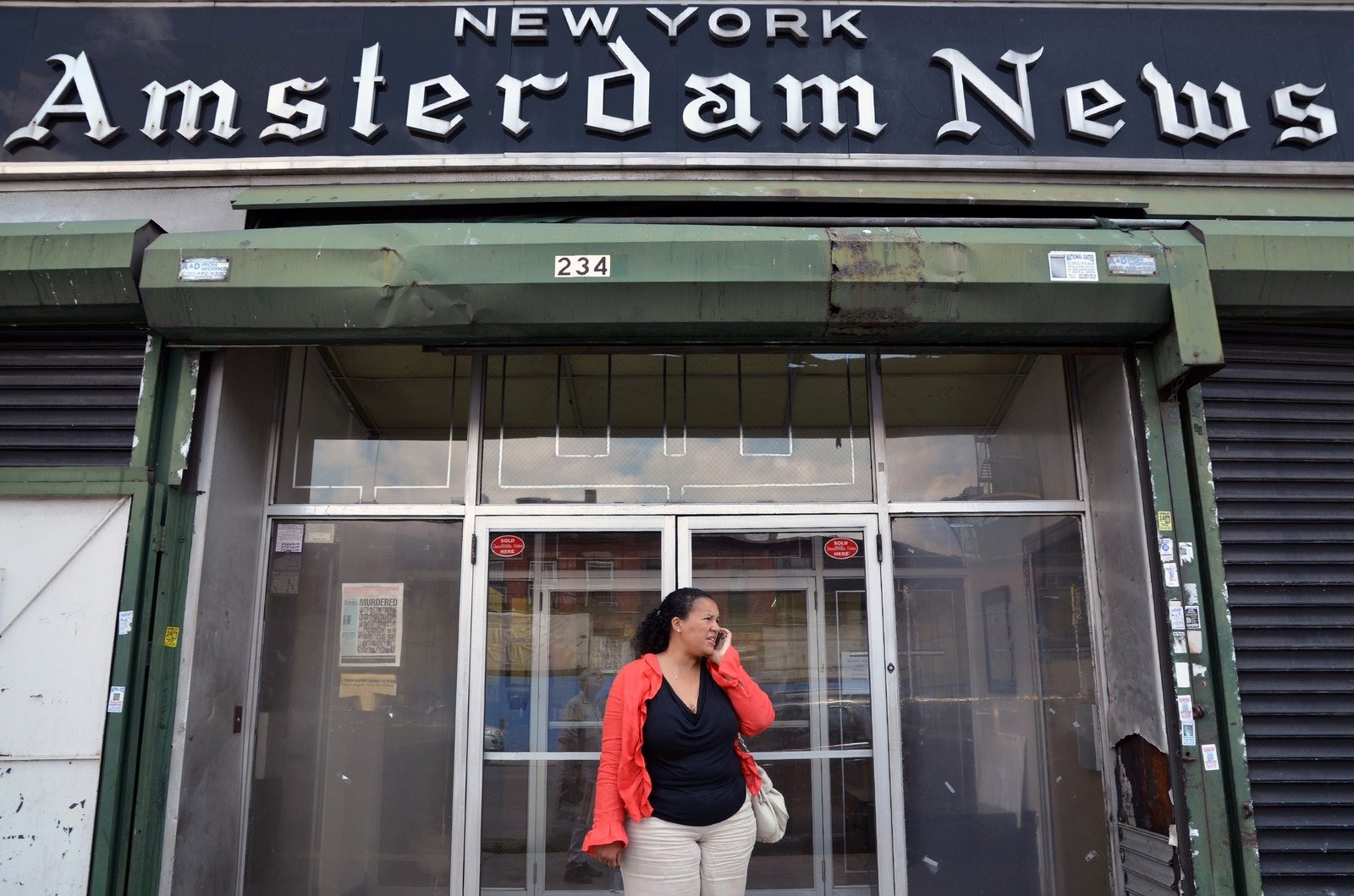 Elinor Tatum, in a red jacket, on the phone in the doorway of the New York Amsterdam News building