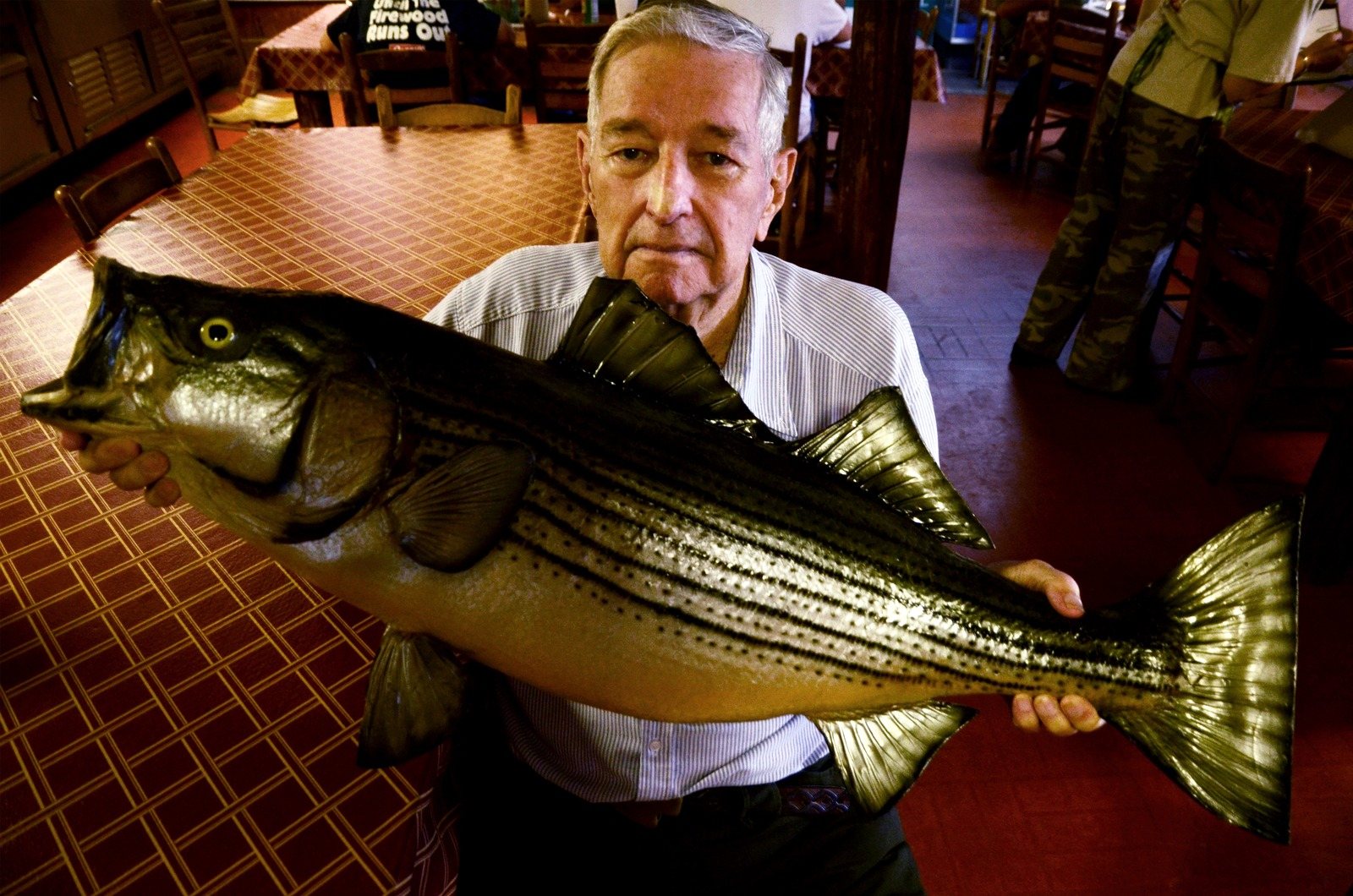 Jack Wingate holds a large mounted striped bass in a restaurant dining room