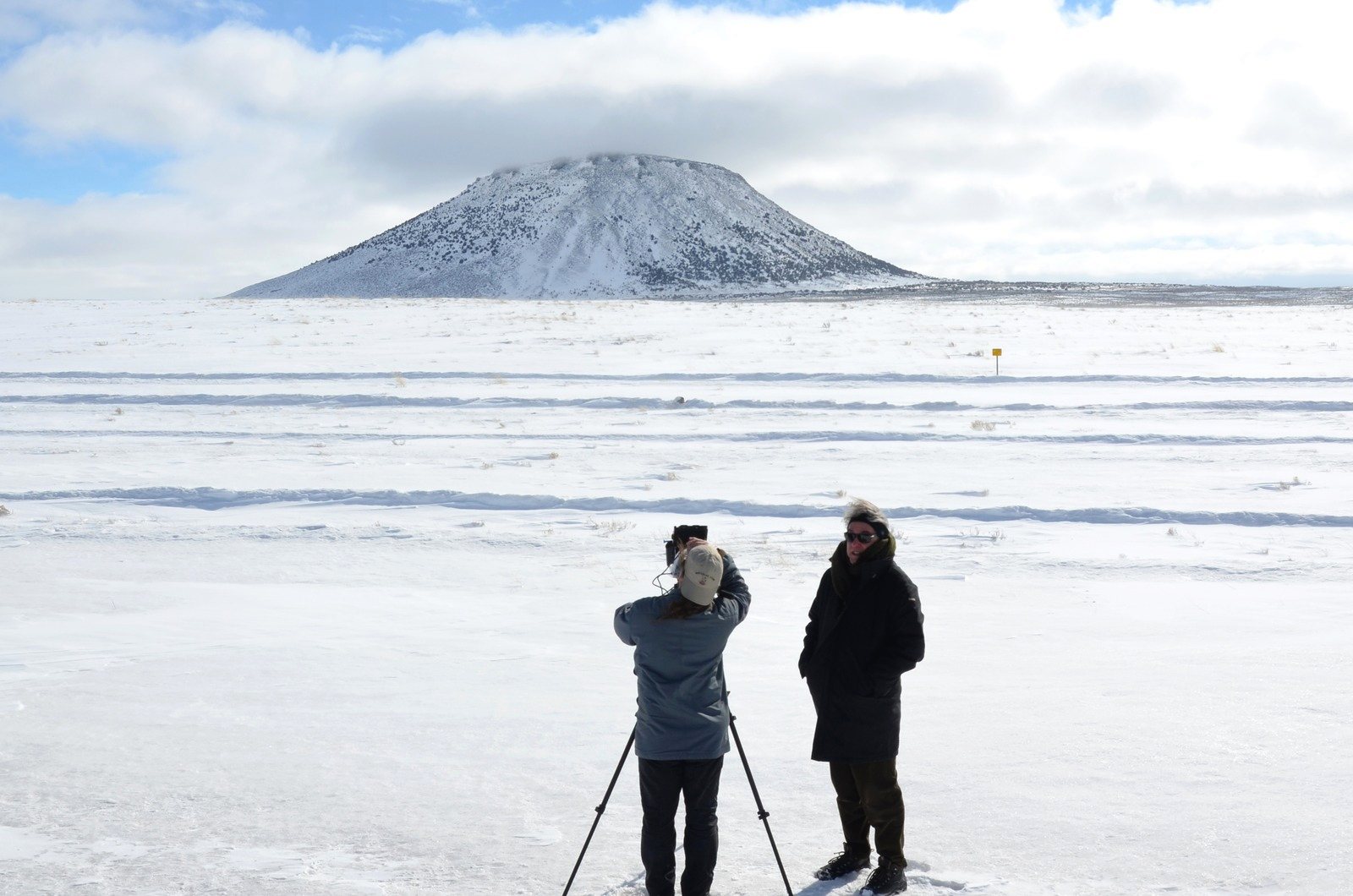 Ben Wolf at a camera on a tripod and Rogier van Eck on a snow-covered plain, a single snowy butte on the horizon