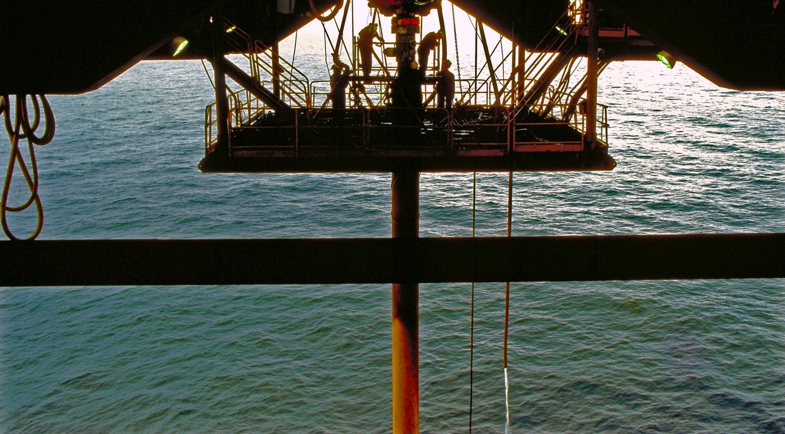 The sea seen from under a platform deck, a gangway and figures silhouetted against the light