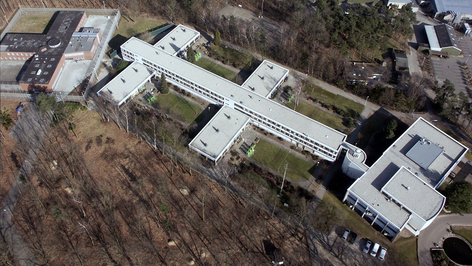 An aerial view of the prison buildings in a cross shape among trees and a car park