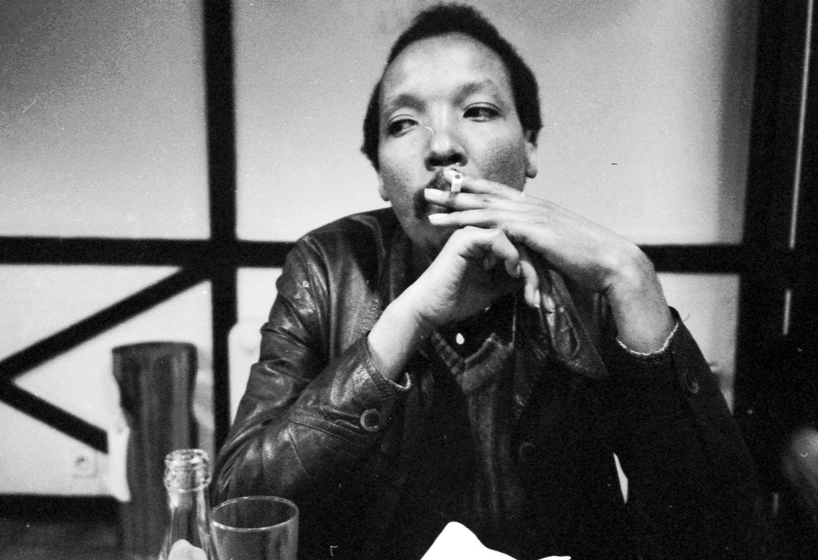Noël N’Tunda smoking, his hands joined in front of his face