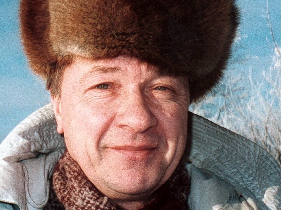 Close portrait of a smiling man in a fur hat, frosted branches behind