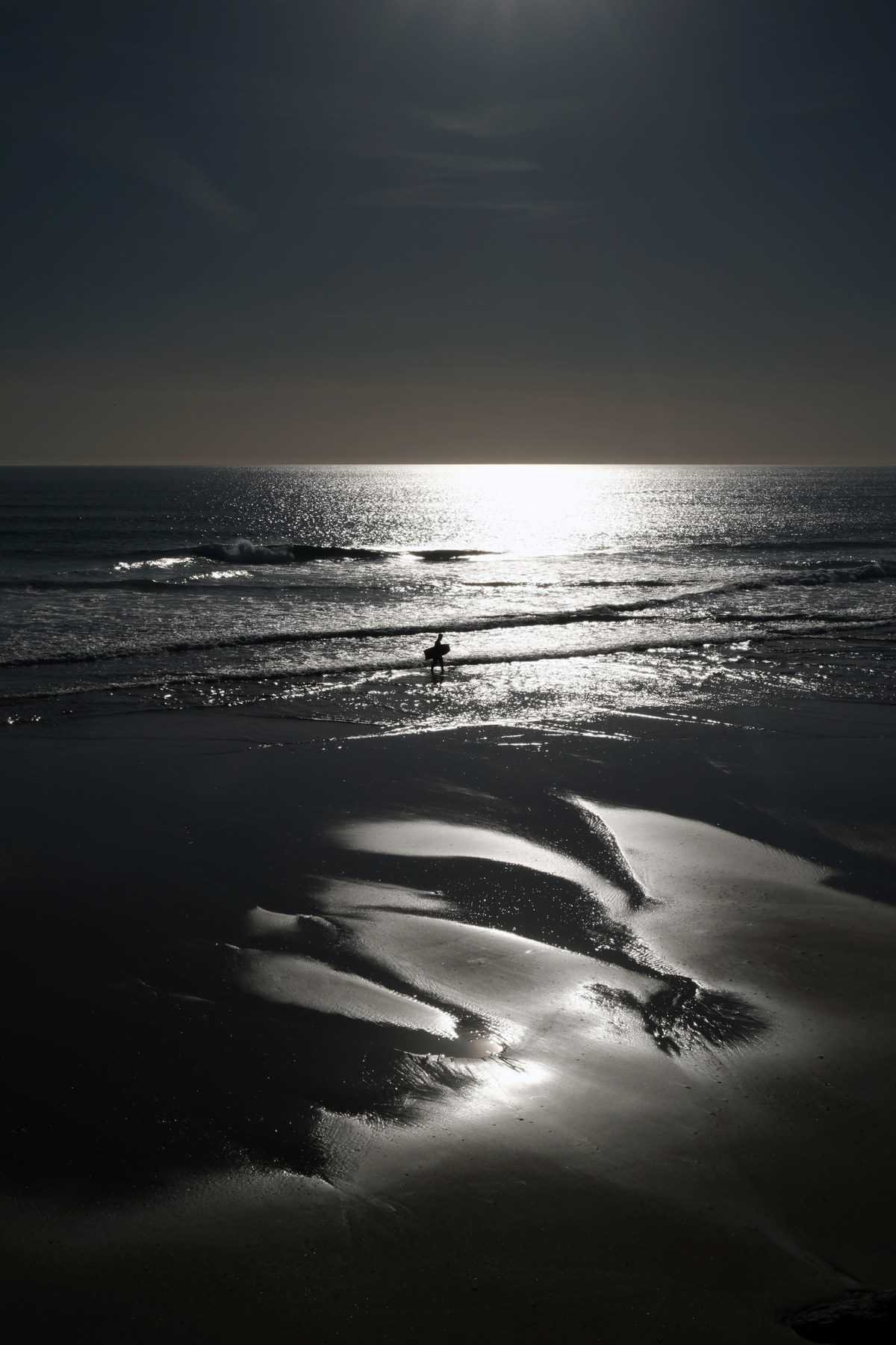 Sunlight on the sea and on wet sand, a small figure in the distance