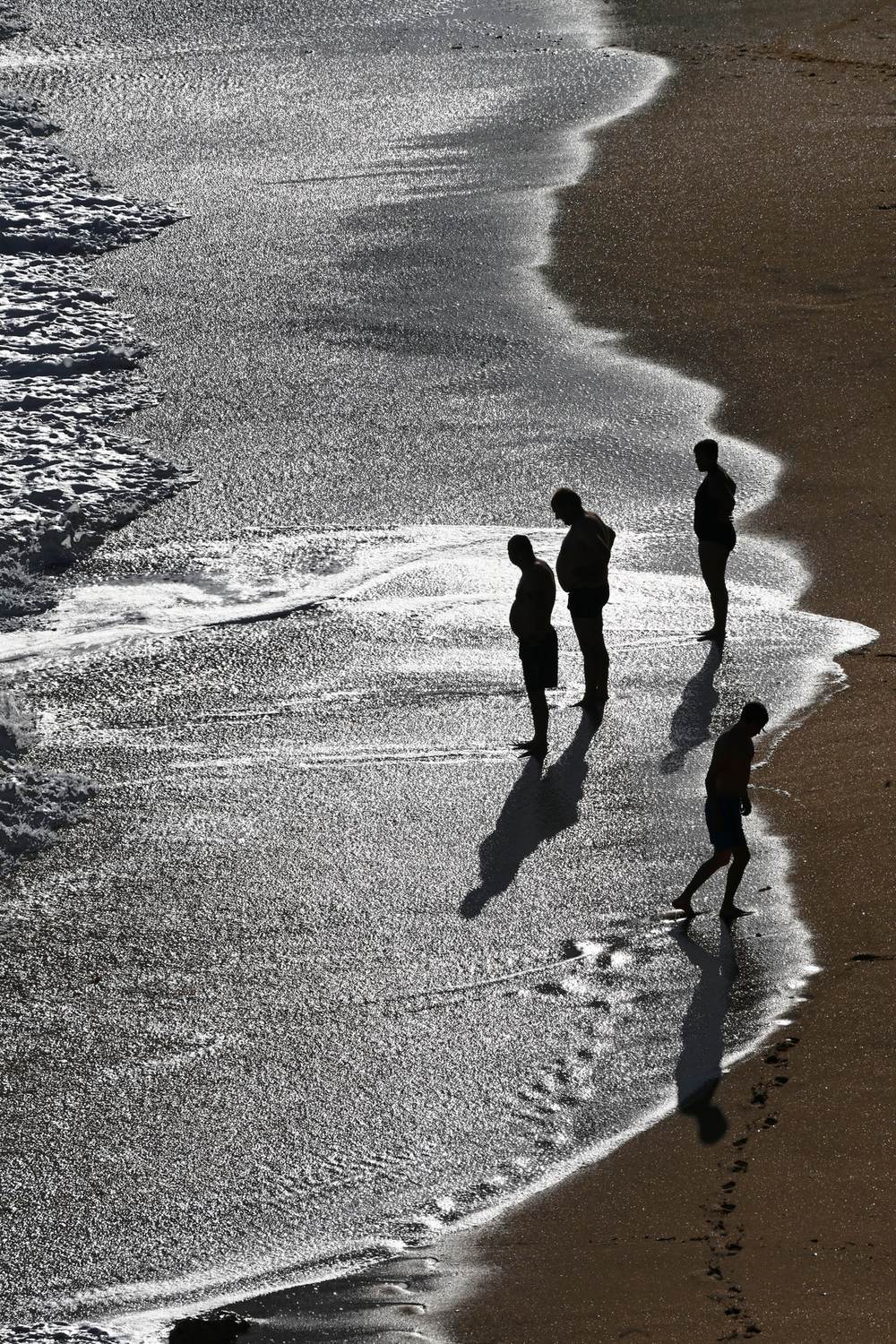 Silhouettes of four people at the edge of the surf, seen from above