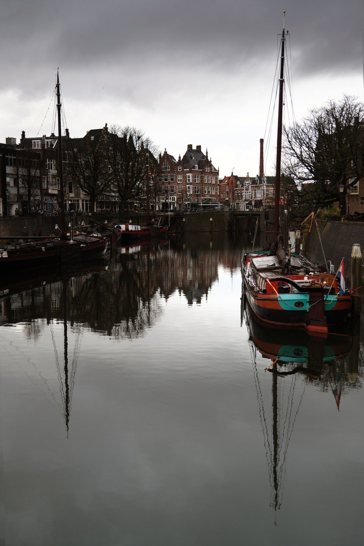 Old sailing boats moored in a harbour under a grey sky