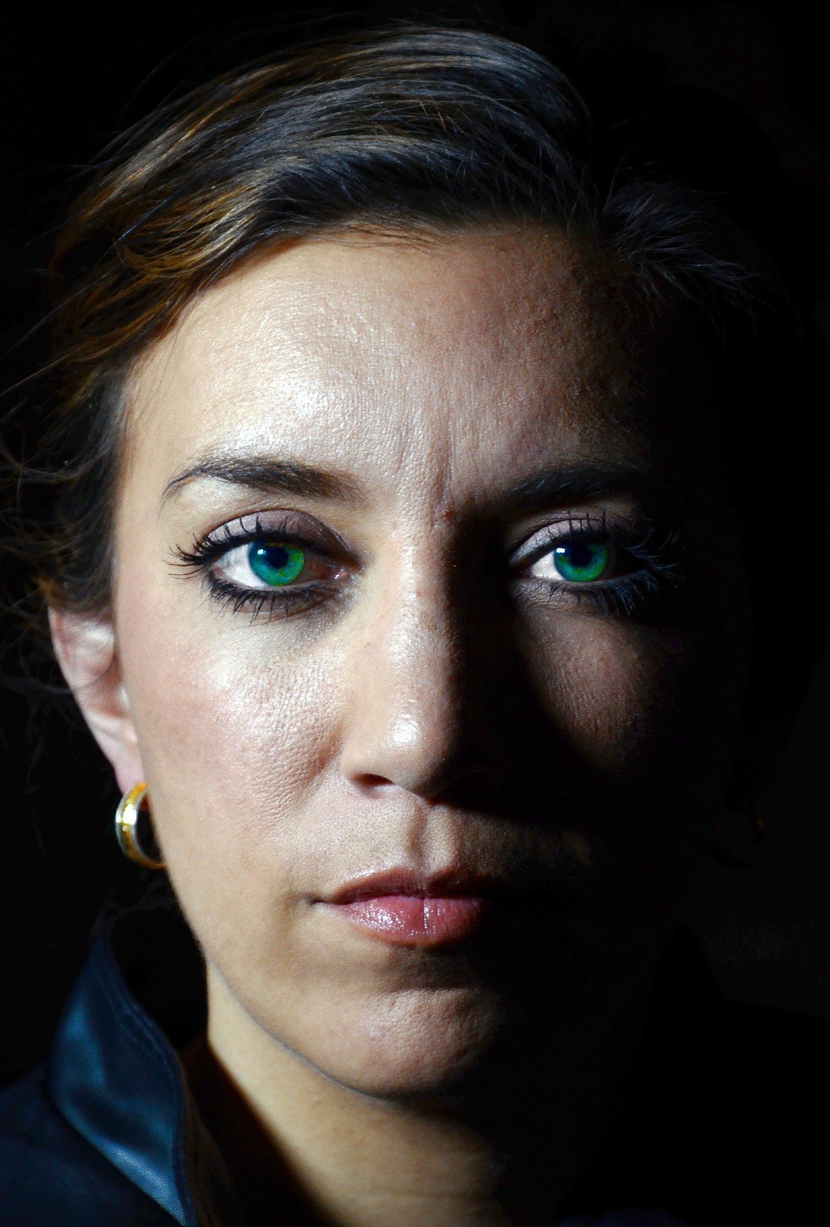 A woman with green eyes and gold earrings, half lit, against a black background