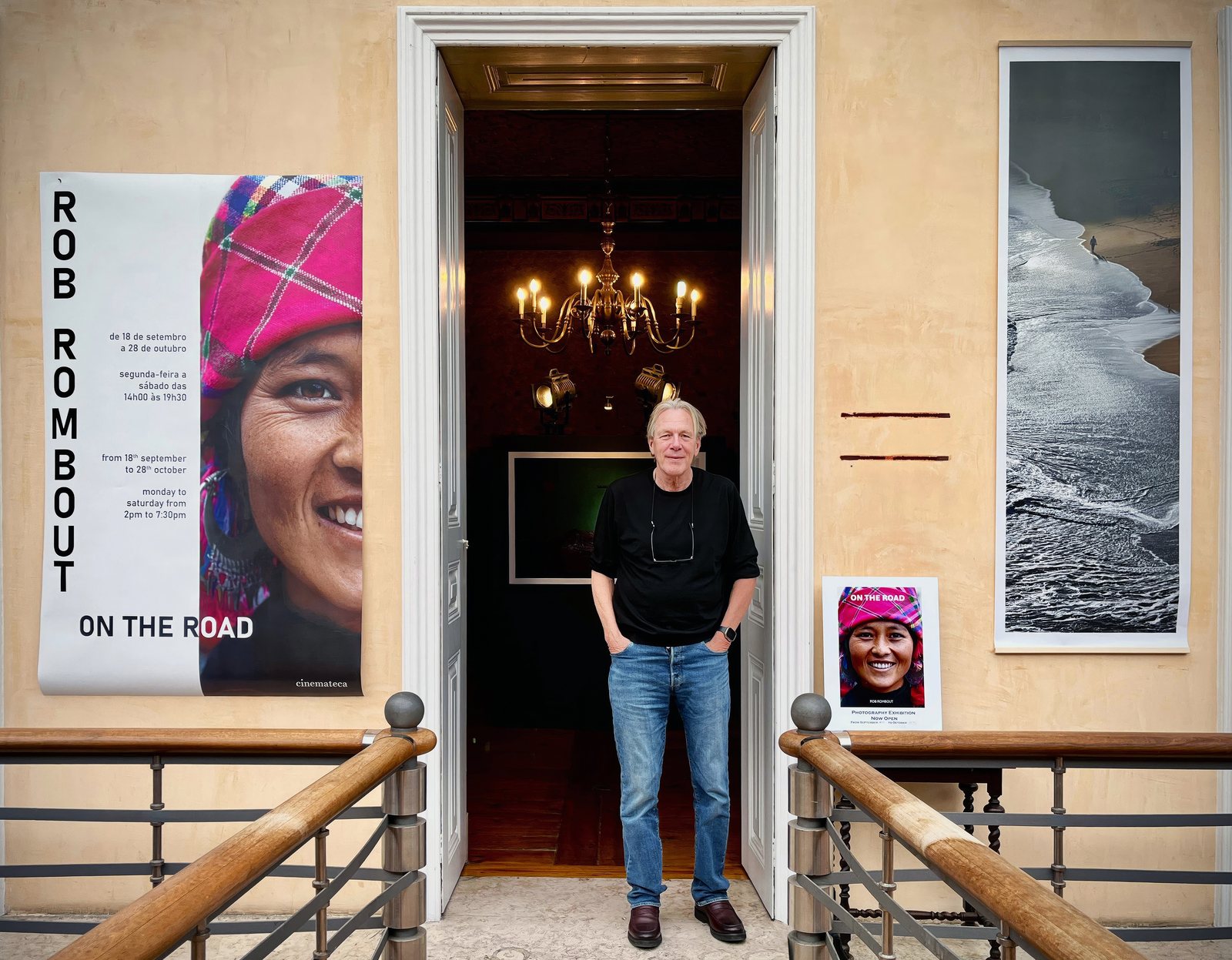 Rob Rombout standing in the doorway of his exhibition, beside a tall poster reading Rob Rombout, on the road