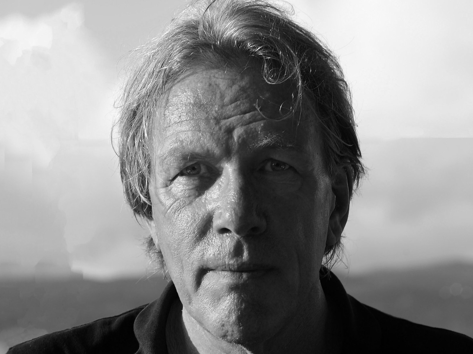 Rob Rombout, black-and-white portrait, looking into the camera, clouds and hills behind