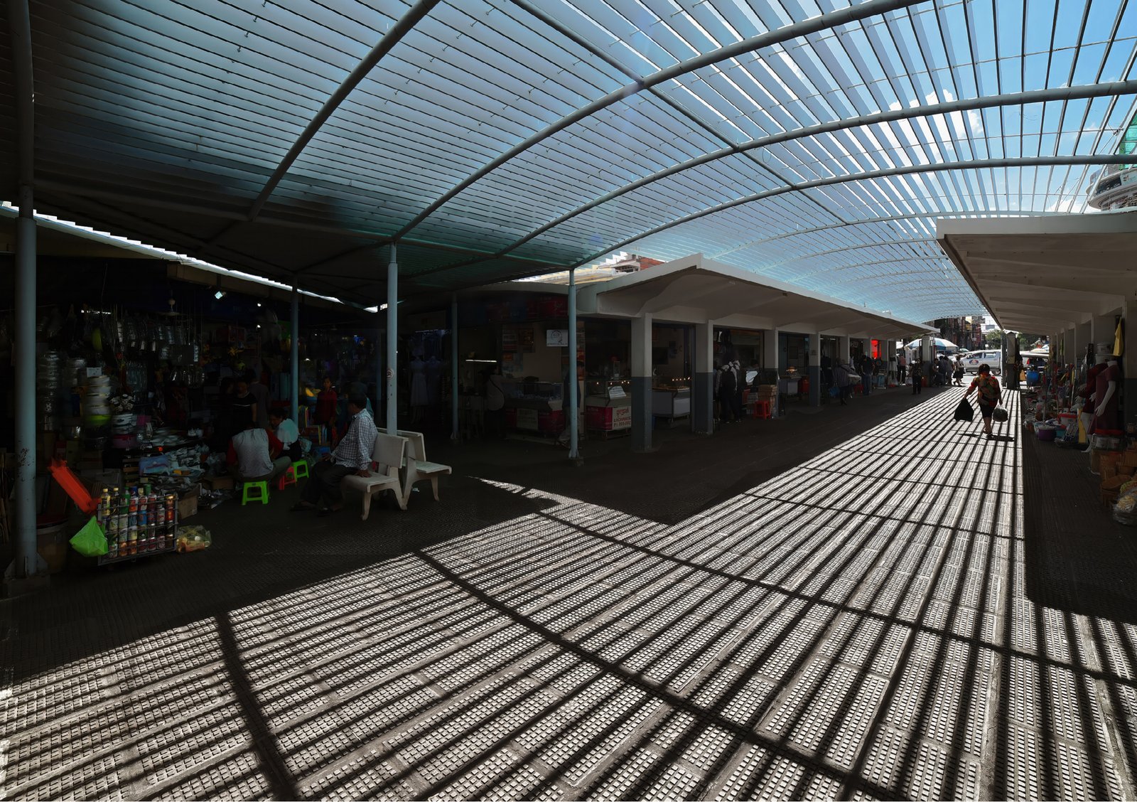 A covered market, the roof casting long stripes of shadow on the ground